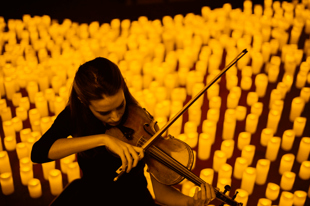 Concert Candlelight. Une femme joue du violon au milieu de centaines de bougies allumées à ses pieds avec un fond noir.