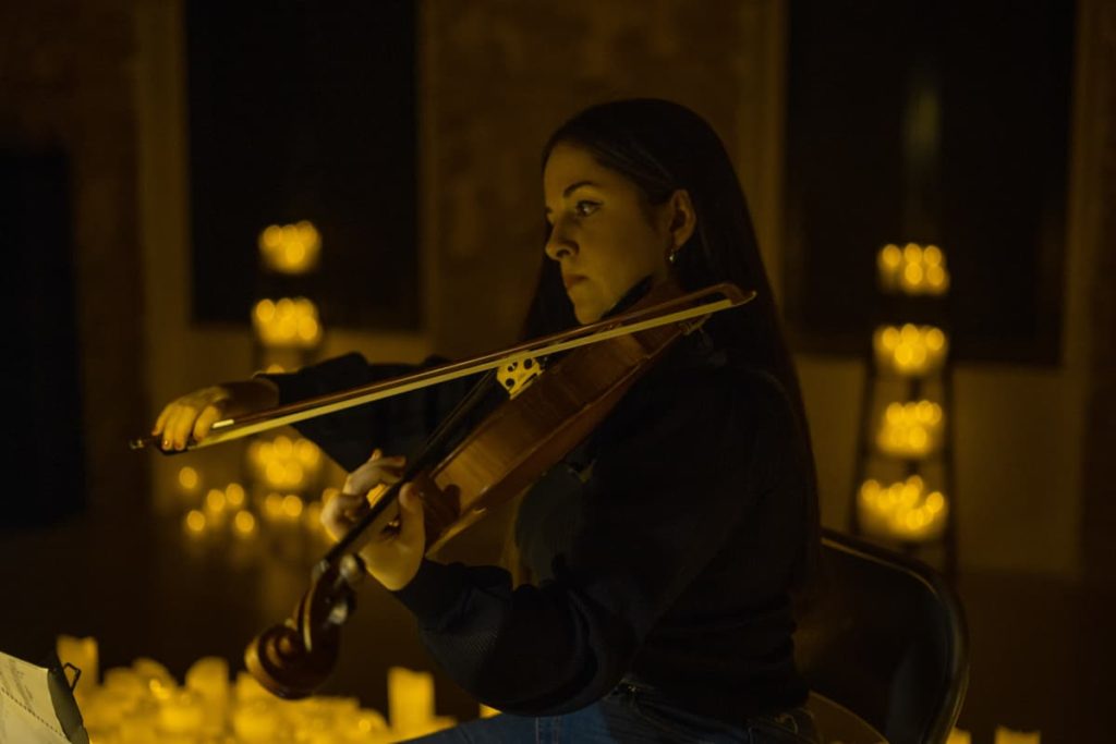 Cocert Candlelight avec une femme qui joue du violon au milieu de l'image. On voit les bougies dans le fond et la lumière reflète son visage