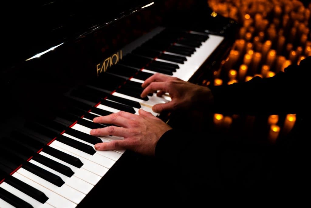 Gros plan sur les mains d'un pianiste et son piano lors d'un Concert Candlelight. On voit des bougies dans le fond